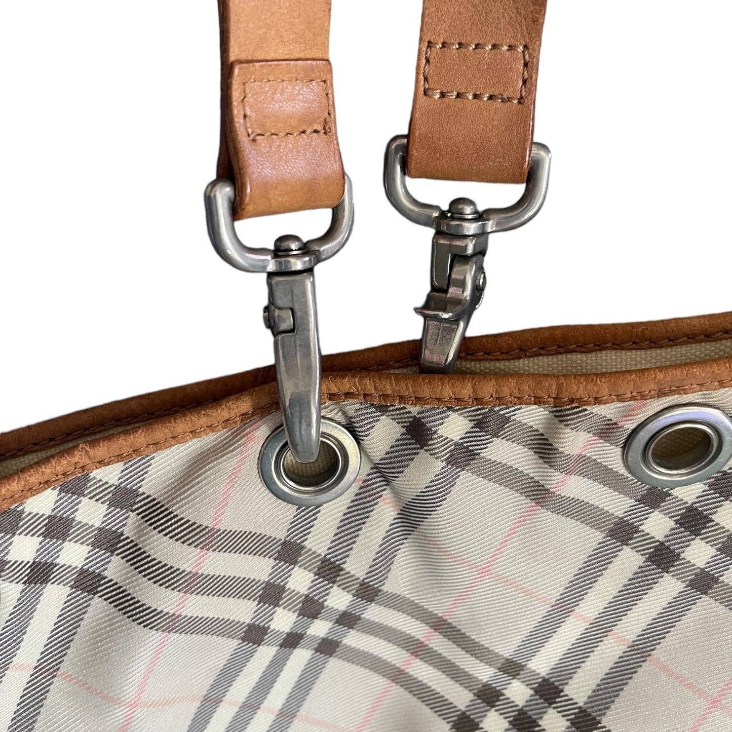 Close-up of a plaid fabric with metal grommets and brown leather straps.