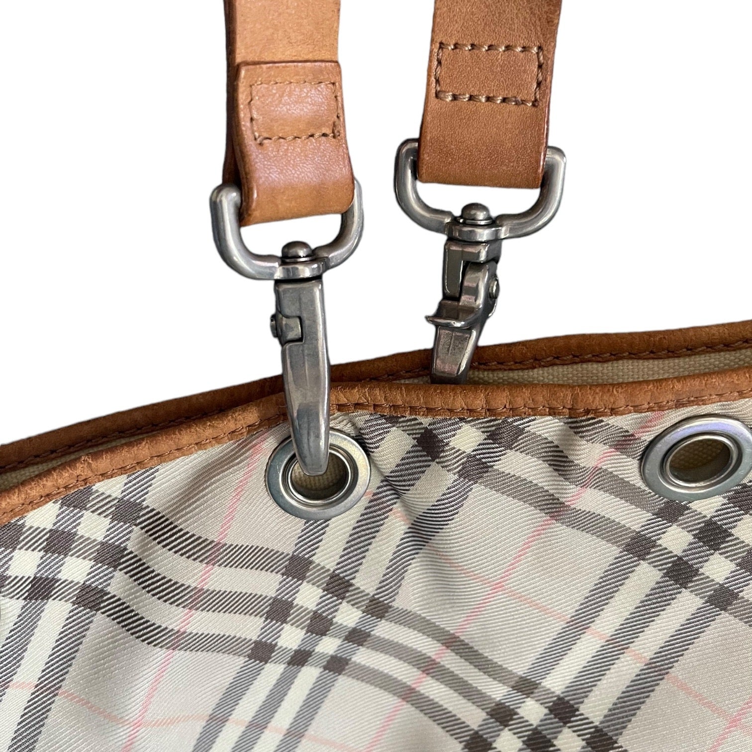 Close-up of a plaid fabric with metal grommets and brown leather straps.