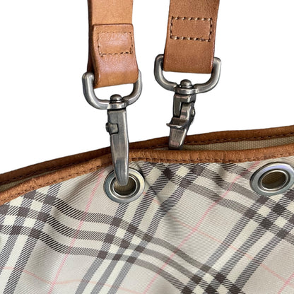 Close-up of a plaid fabric with metal grommets and brown leather straps.