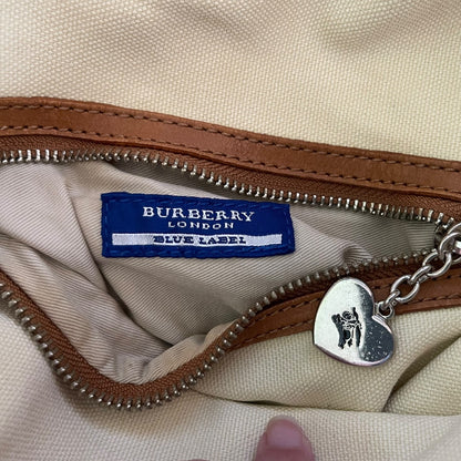 Close-up of a Burberry London Blue Label tag on a beige fabric background with a heart-shaped metal charm.