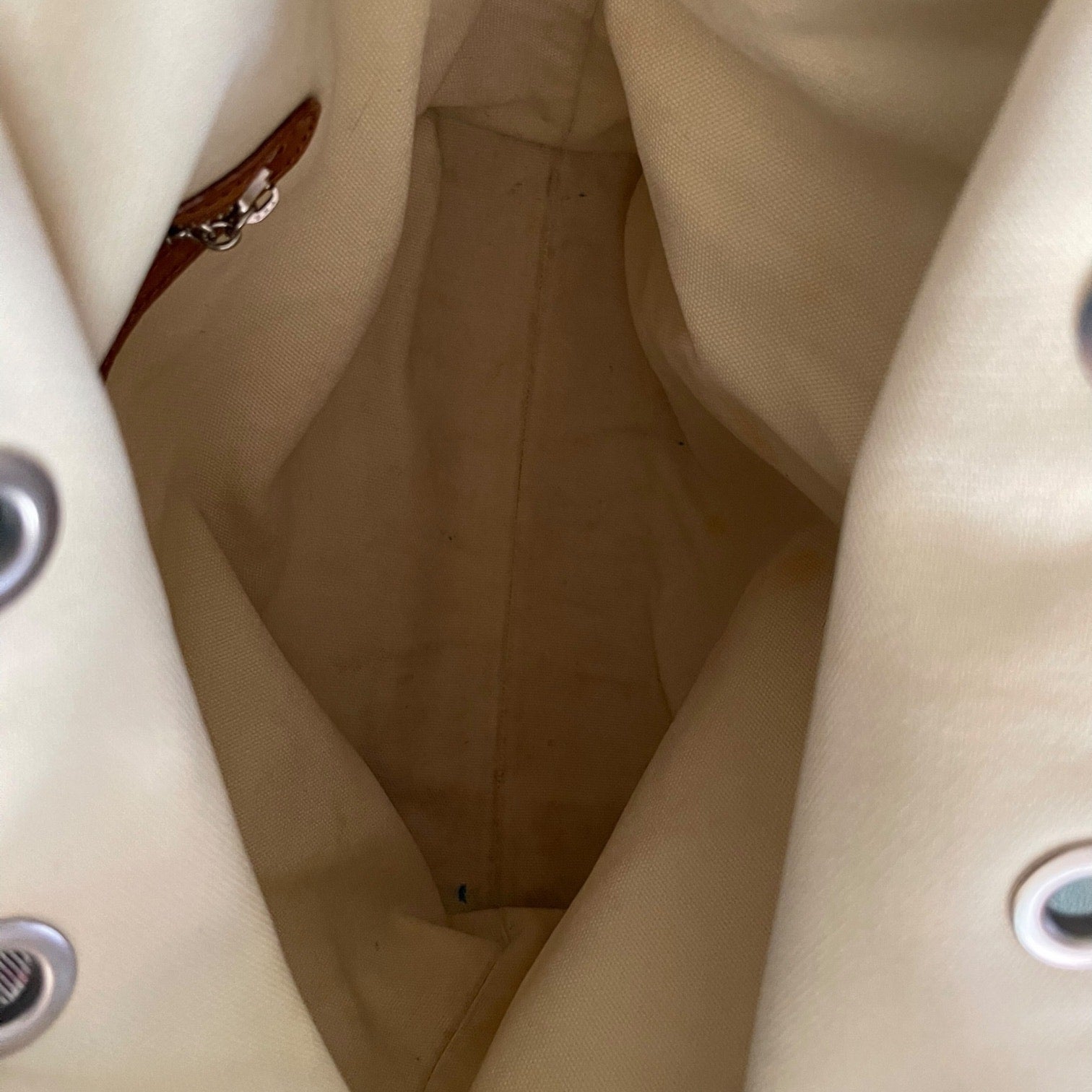 Close-up of a beige fabric interior with a zipper and metal buttons.