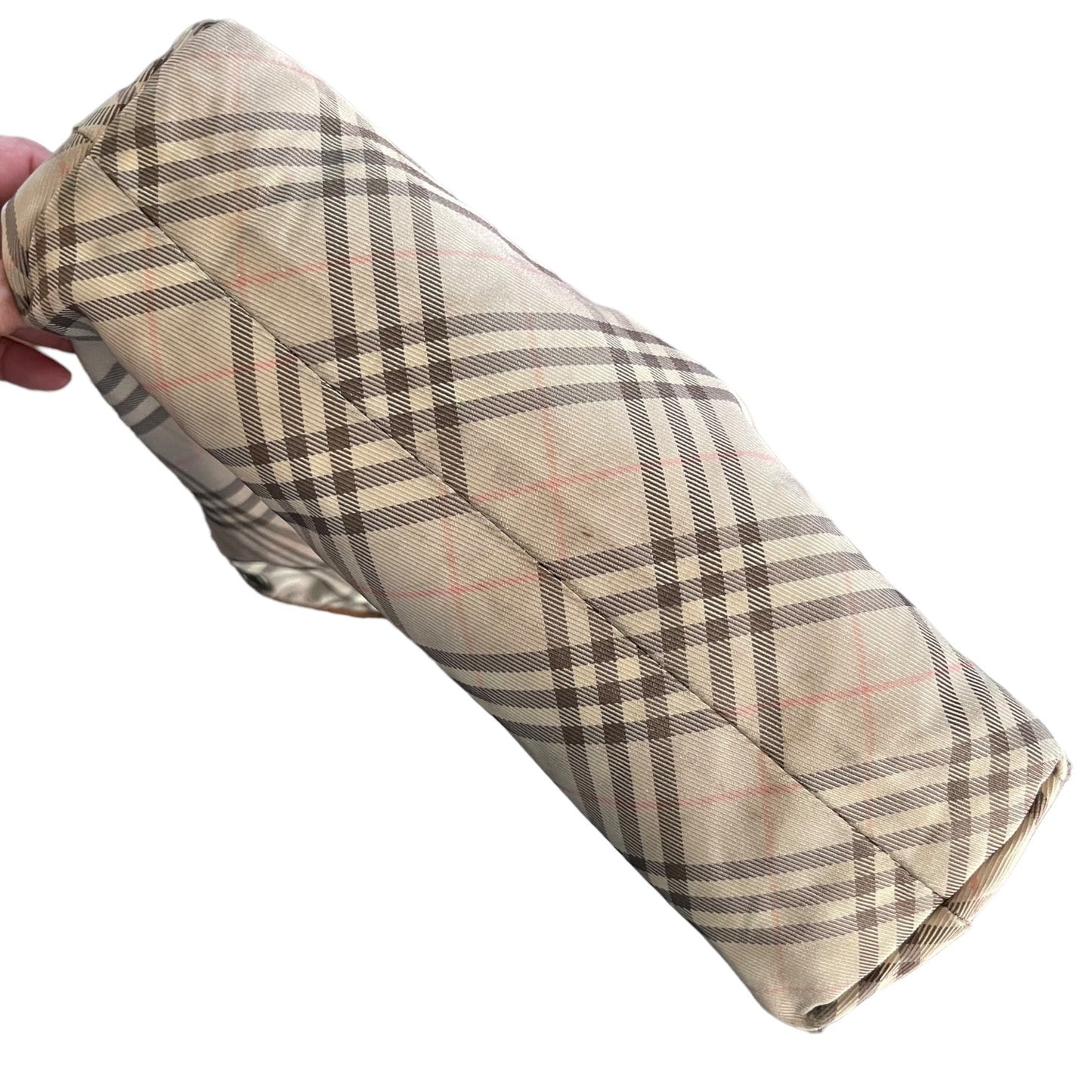 Bottom of purse in a classic check pattern in brown, black, and thin pink lines, held by a hand against a plain white background.