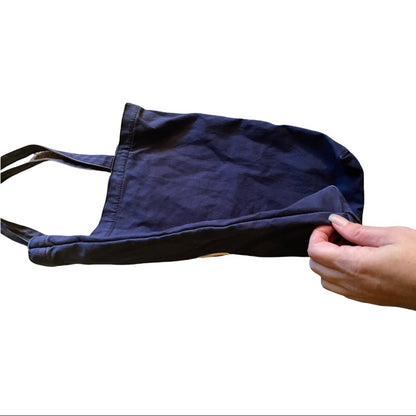 Navy blue tote bag sides held by a hand on a white background