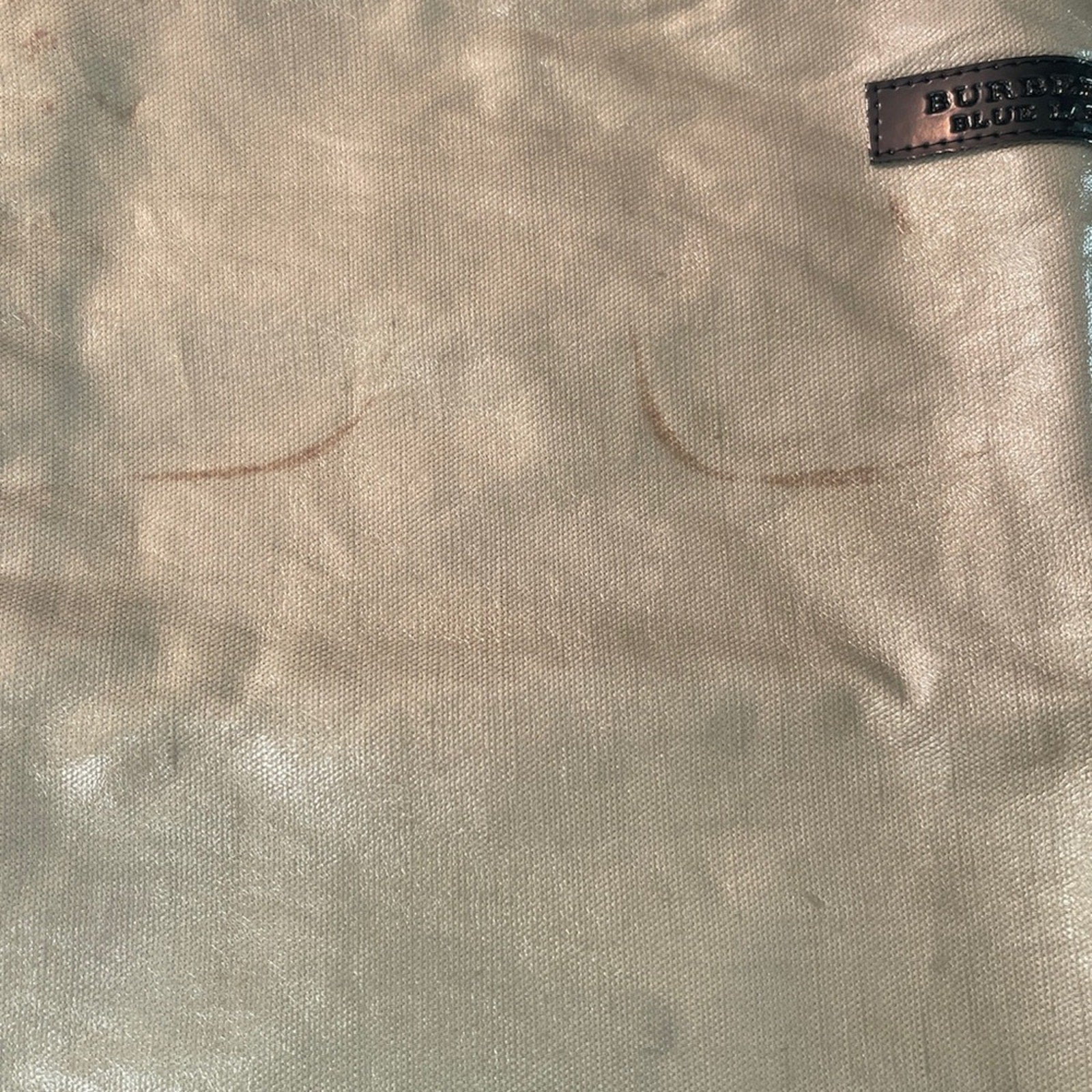 Close-up of beige fabric with a Burberry label in the corner with marks on pouch