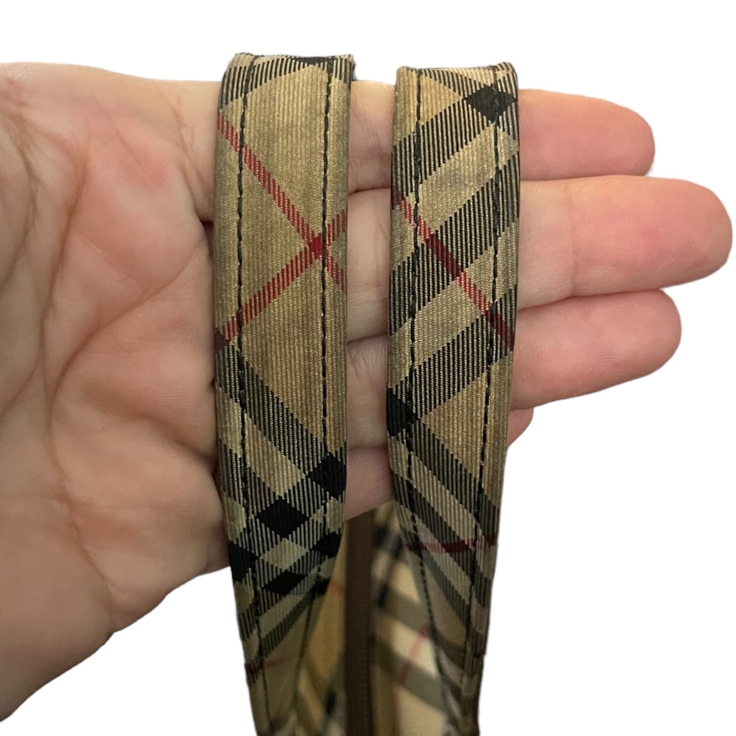 Hand holding two plaid handles with a beige, black, and red pattern.