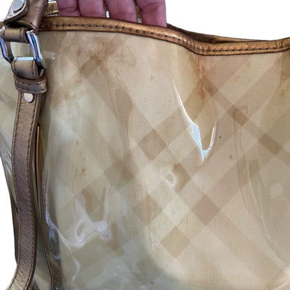 A close-up of a translucent beige and tan checkered handbag with a gold leather strap and trim, held by a hand at the top.
