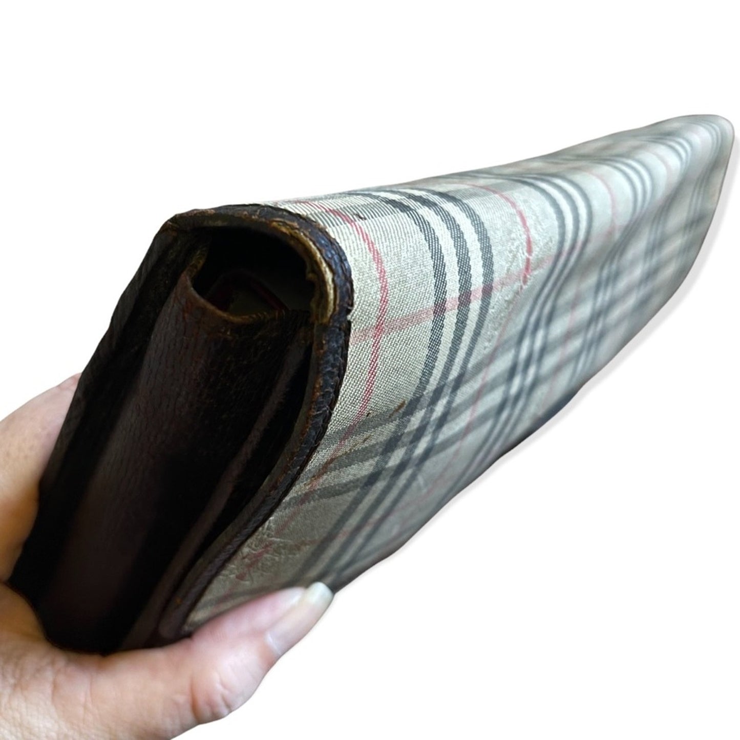 A vintage plaid clutch held in a hand against a plain white background. The wallet features a beige canvas body showing issues on the edge