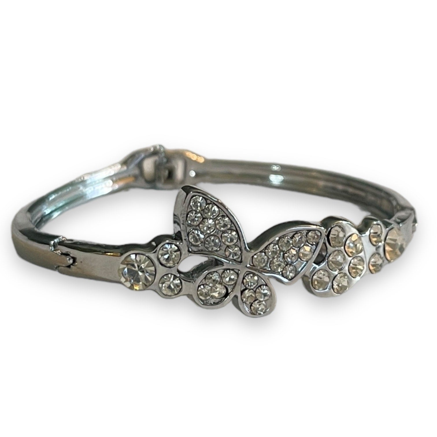 A silver-toned bangle bracelet featuring a butterfly and floral motif embellished with clear rhinestones, set against a plain white background.