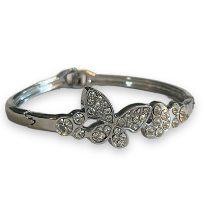 A silver-toned bangle bracelet featuring a butterfly and floral motif embellished with clear rhinestones, set against a plain white background.