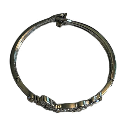 Top view of a polished silver-toned bangle bracelet with a decorative pavé crystal section on one side, shown against a plain white background.