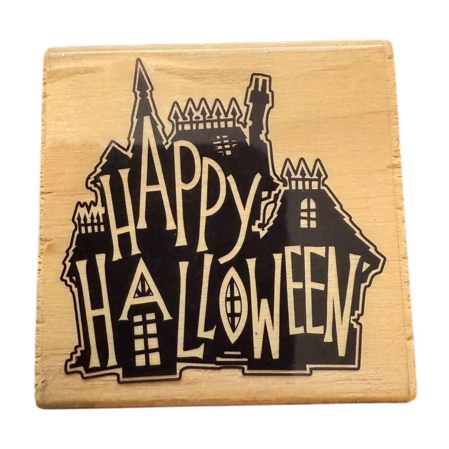 Wooden block with a black silhouette of a haunted house and 'Happy Halloween' text on a white background