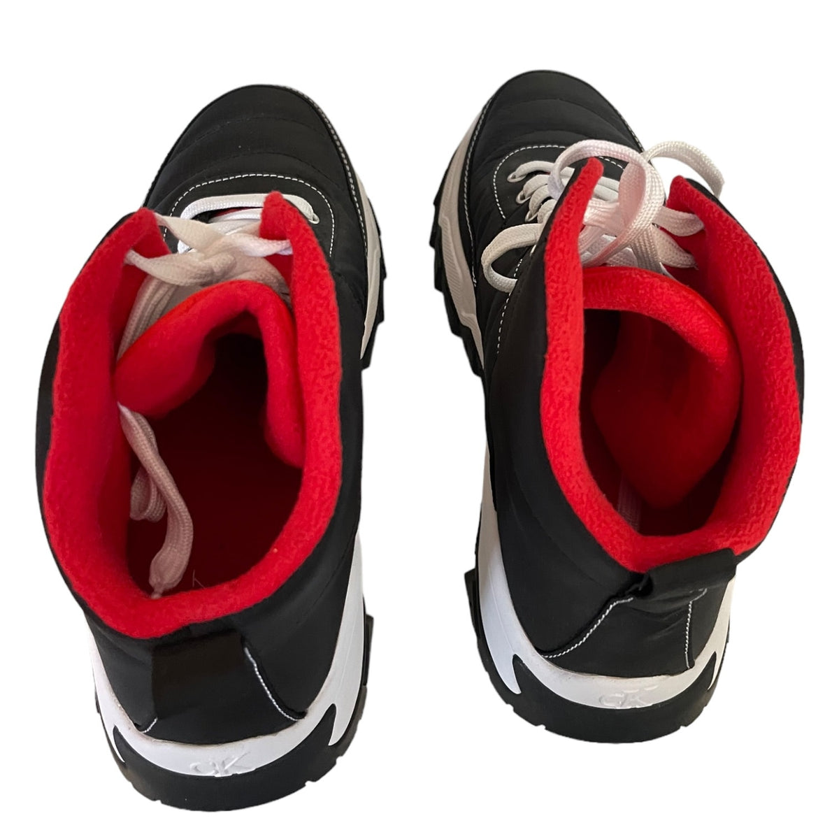 A pair of black sneakers with bright red fleece lining and white laces, shown from a top-down view on a white background.