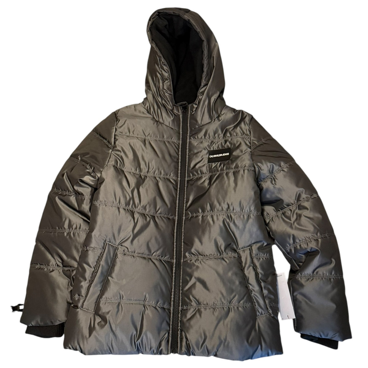 A dark gray hooded puffer jacket with horizontal quilting, a front zipper, and a small black-and-white logo patch on the chest, shown against a plain white background.