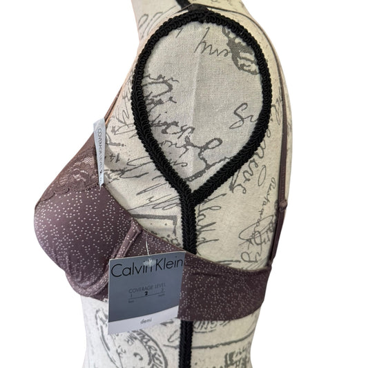 A Calvin Klein coverage bra in a dusty mauve color with white micro-spots , displayed on a patterned dress form against a white background.