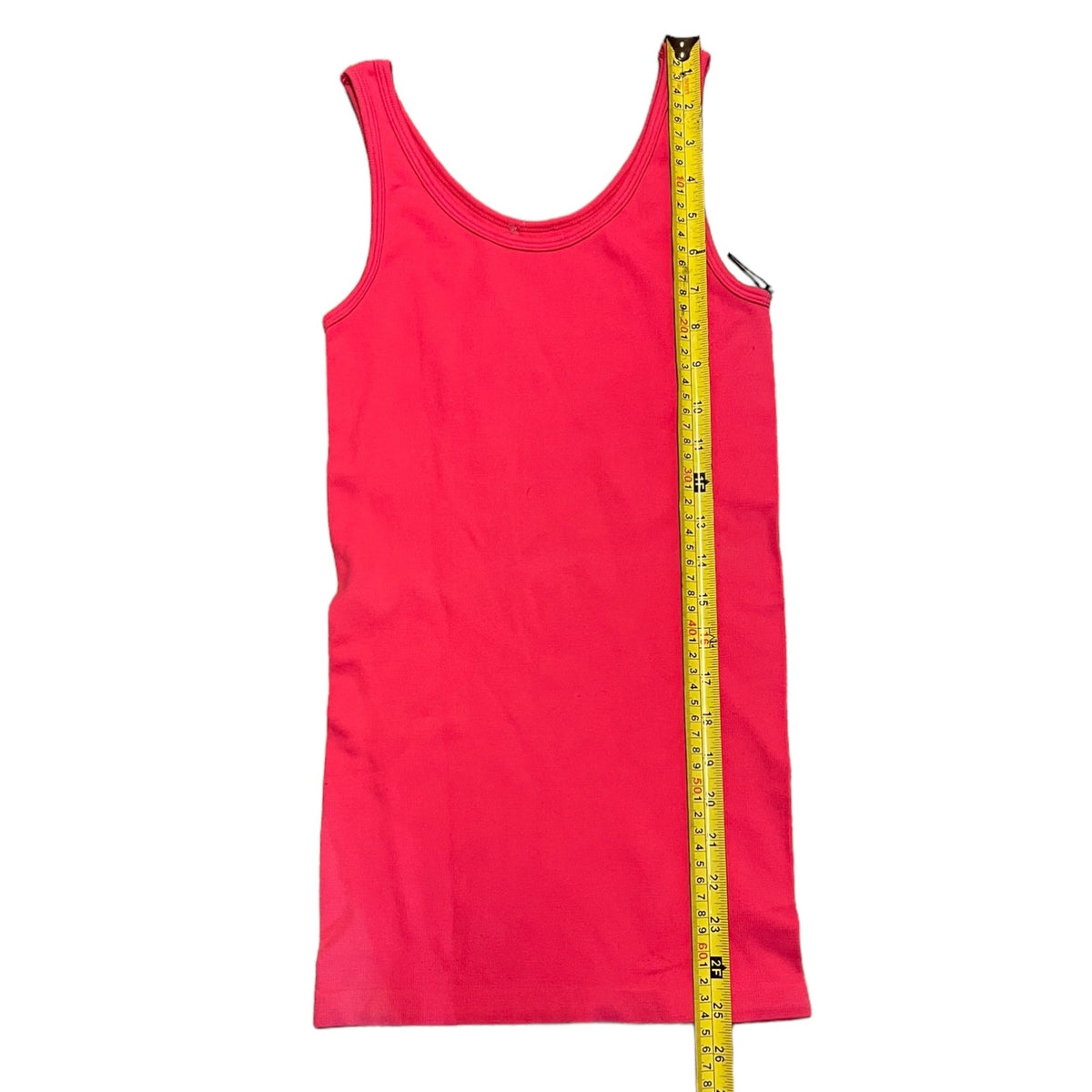 A bright pink sleeveless tank top laid flat on a white background, with a yellow tape measure standing vertically along the right side to show its height.