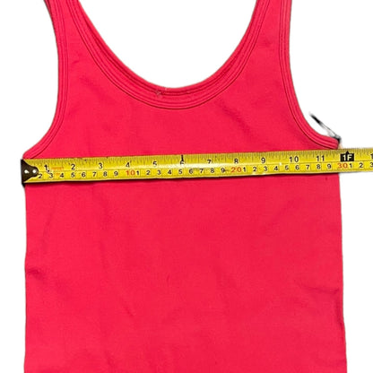 A bright pink tank top laid flat on a white background with a yellow tape measure stretched horizontally across the chest to show the width measurement.