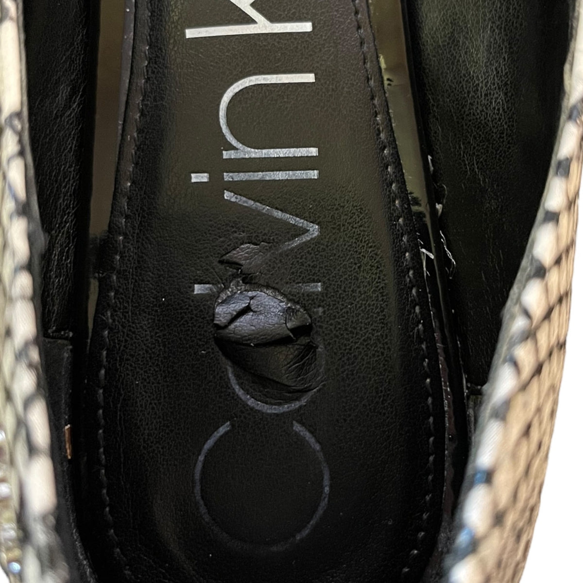 Close-up of a Calvin Klein shoe insole with the brand name printed vertically, surrounded by a snakeskin-patterned material.
