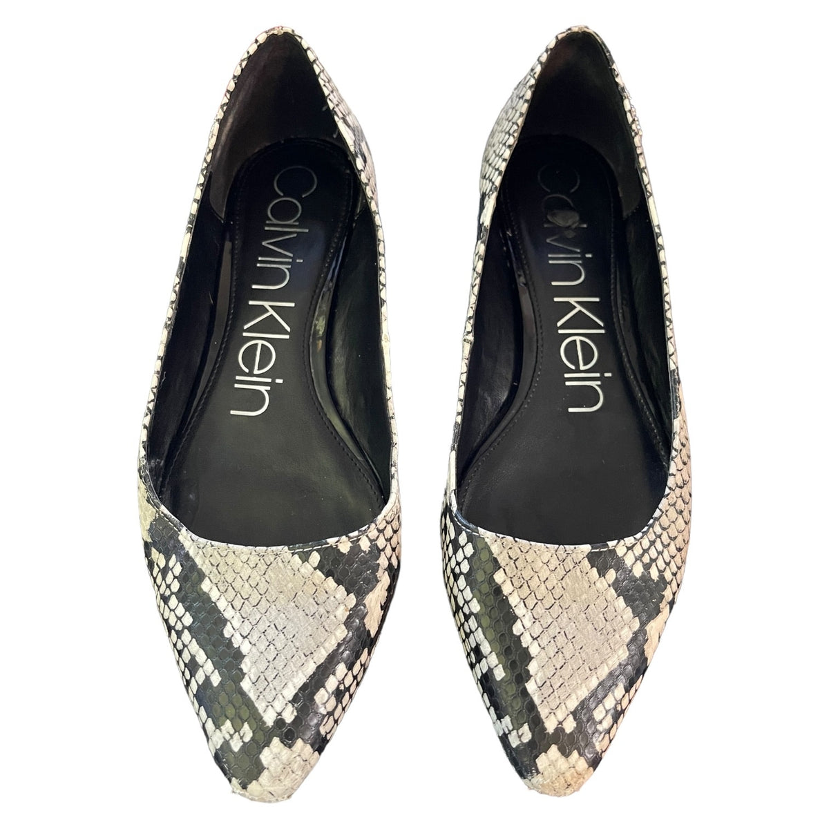 A pair of Calvin Klein pointed-toe pumps featuring a snakeskin pattern in beige, gray, and black, with the brand name printed in white on the black insoles.