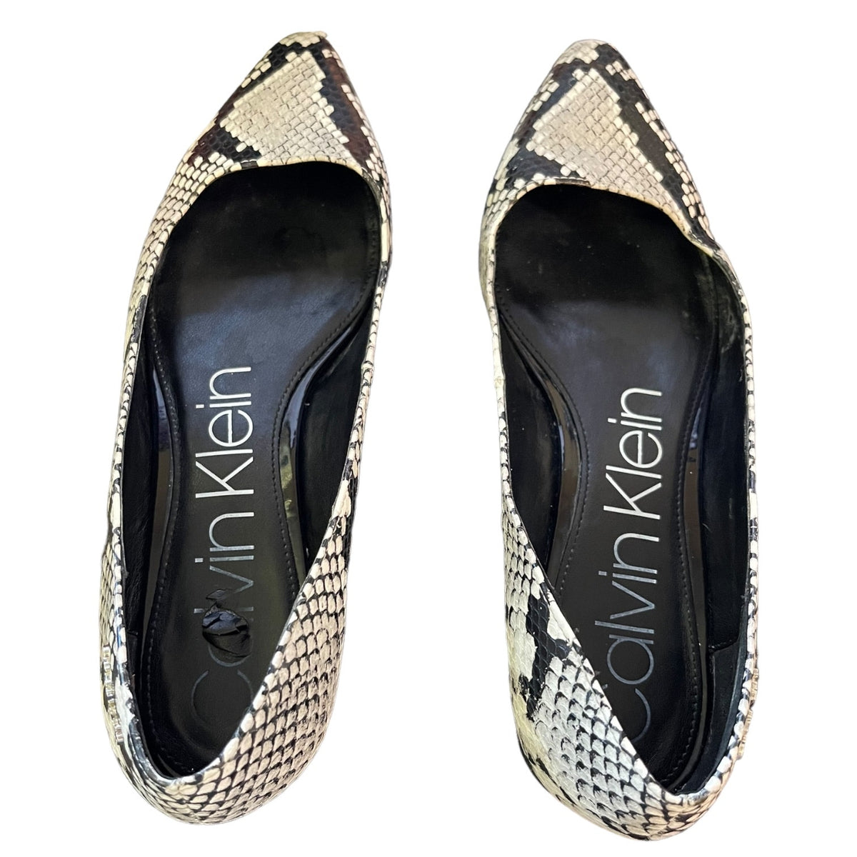 A pair of Calvin Klein pointed-toe flats featuring a beige, black, and white snakeskin pattern, shown from a top-down view on a white background.