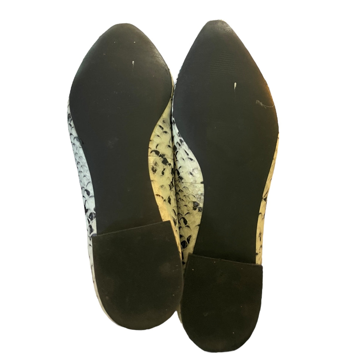 A pair of pointed-toe flats shown from the bottom, featuring a black rubber sole and heel counter with a black, white, and snakeskin patterned upper.