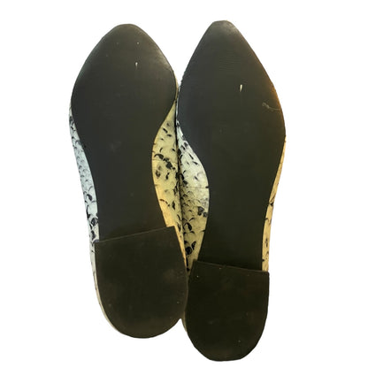 A pair of pointed-toe flats shown from the bottom, featuring a black rubber sole and heel counter with a black, white, and snakeskin patterned upper.