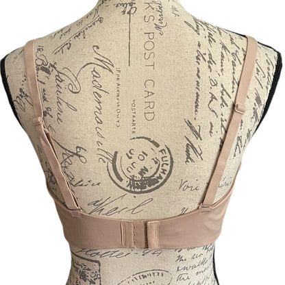 Back of a tan bra with adjustable shoulder straps and a wide front band, displayed on a vintage-style printed fabric dress form mannequin against a white background.