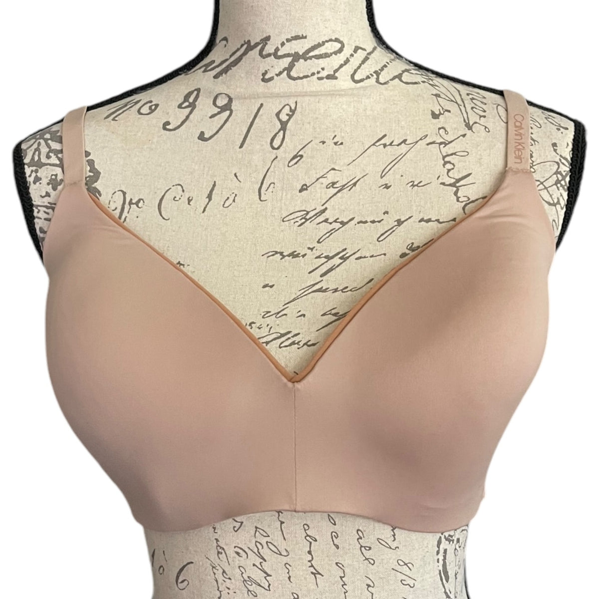 A light tan wireless bra displayed on a patterned mannequin torso against a white background.