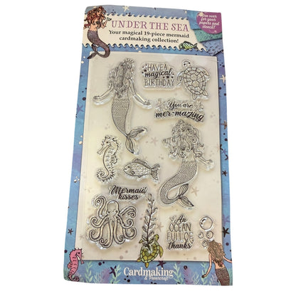 Mermaid-themed cardmaking collection stamp set in its retail packaging, featuring clear stamps of mermaids, a turtle, an octopus, a seahorse, bubbles, and sea plants with phrases like 'Have a magical birthday' and 'You are mermaidly'.