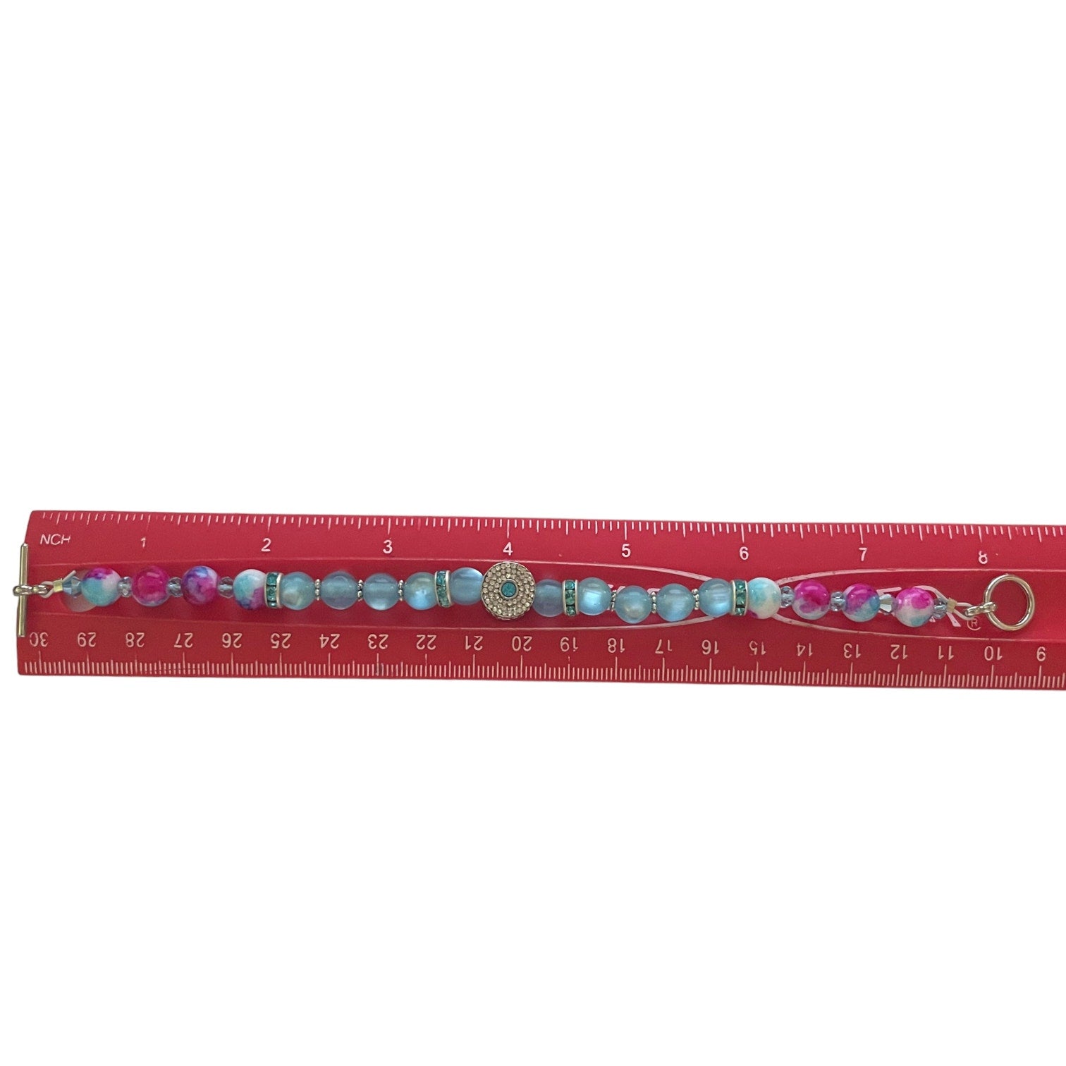 Bracelet with colorful beads and charm on a red ruler for scale.