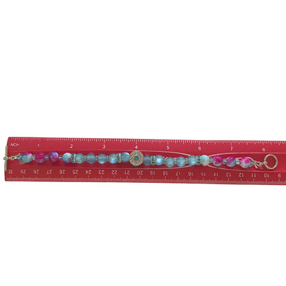 Bracelet with colorful beads and charm on a red ruler for scale.