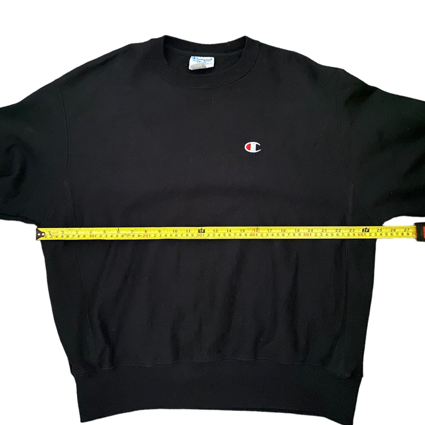 Black sweatshirt with a small logo being measured by a yellow tape measure on a white background