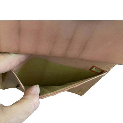 Close-up of a hand holding an open a brown pocket on a pink wallet with a white background