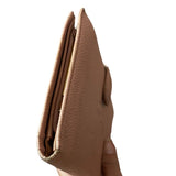 Corners of pink leather wallet held by a hand on a white background
