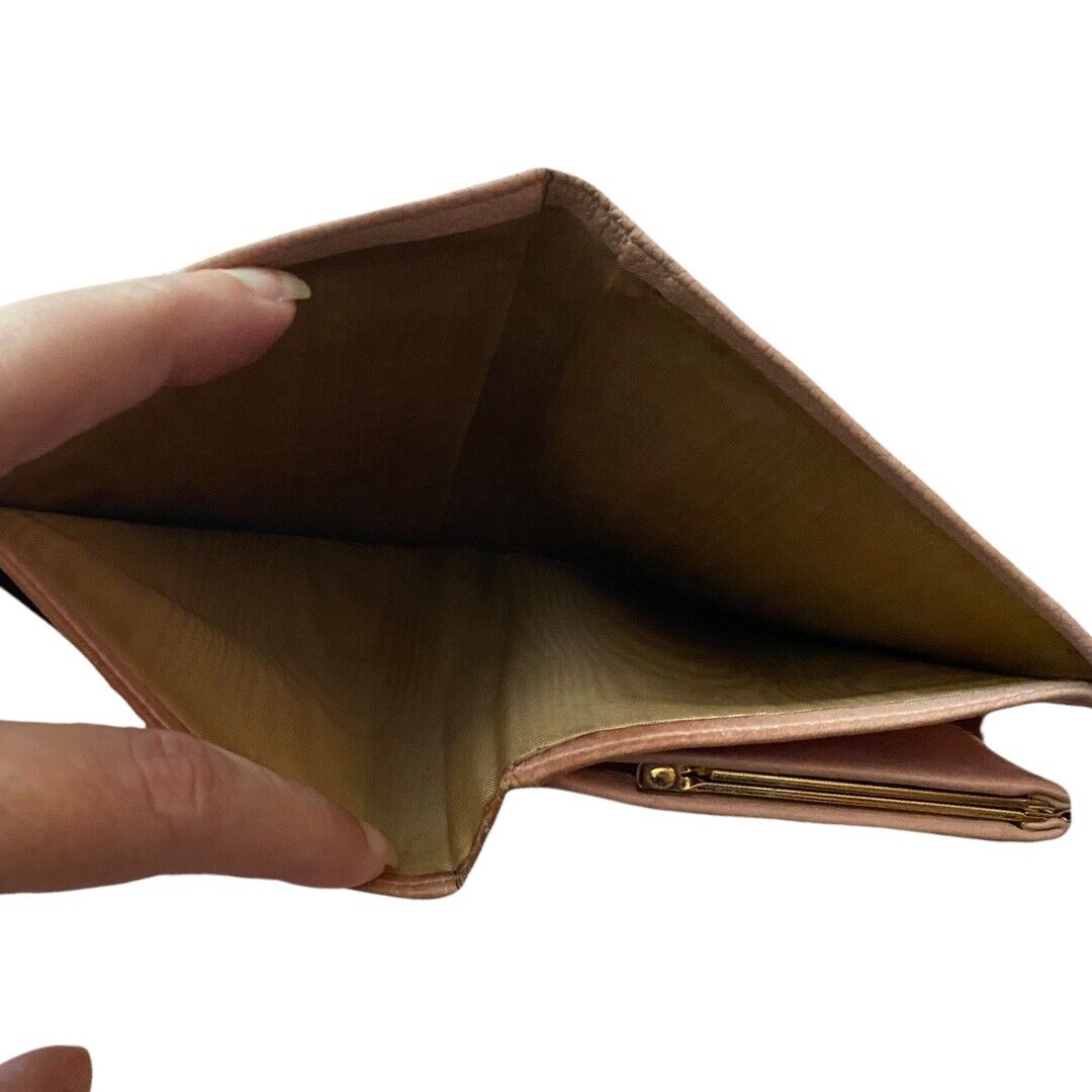 Pink leather wallet held open by a hand, brown interior on a white background