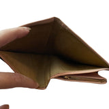 Pink leather wallet held open by a hand, brown interior on a white background