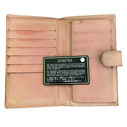 An open Chanel leather wallet in a light PINK, showing multiple card slots, and a black card insert with white text. The Chanel logo is subtly printed in gold near the bottom left corner.