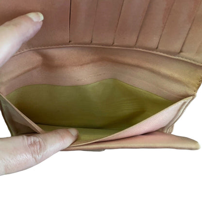 Close-up of a pink leather wallet with a brown interior pocket, held open by a hand.