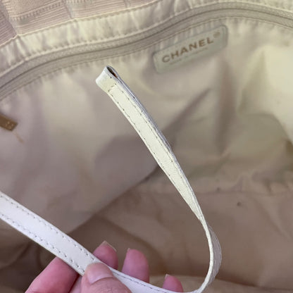 Close-up of a Chanel handbag interior with a cream-colored leather strap held by a hand, showing the CHANEL label stitched inside the lining.