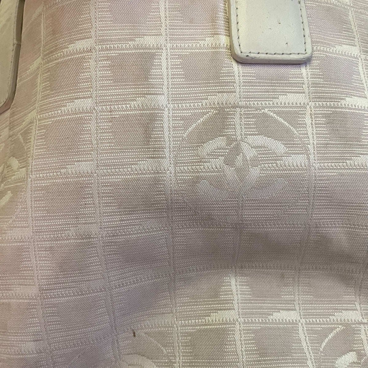 Close up of a CC grid pattern on a off white beige purse with light marks and stains. 