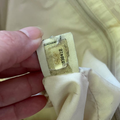 A close-up of a hand holding a beige fabric tag with a clear plastic window showing the printed Chanel logo and item number .