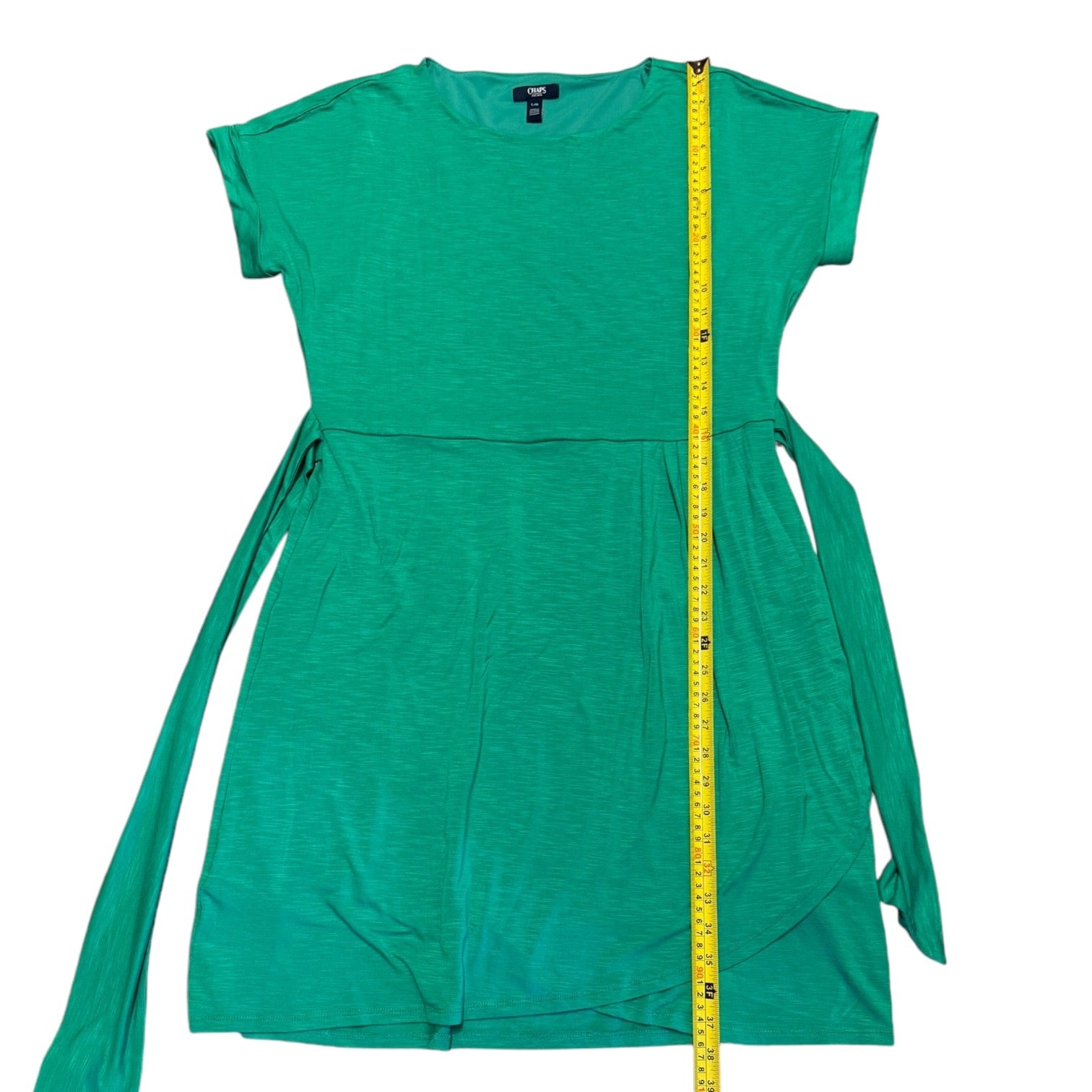 A green short-sleeve dress with side ties, shown flat on a white background with a yellow measuring tape running vertically down the center to indicate size.