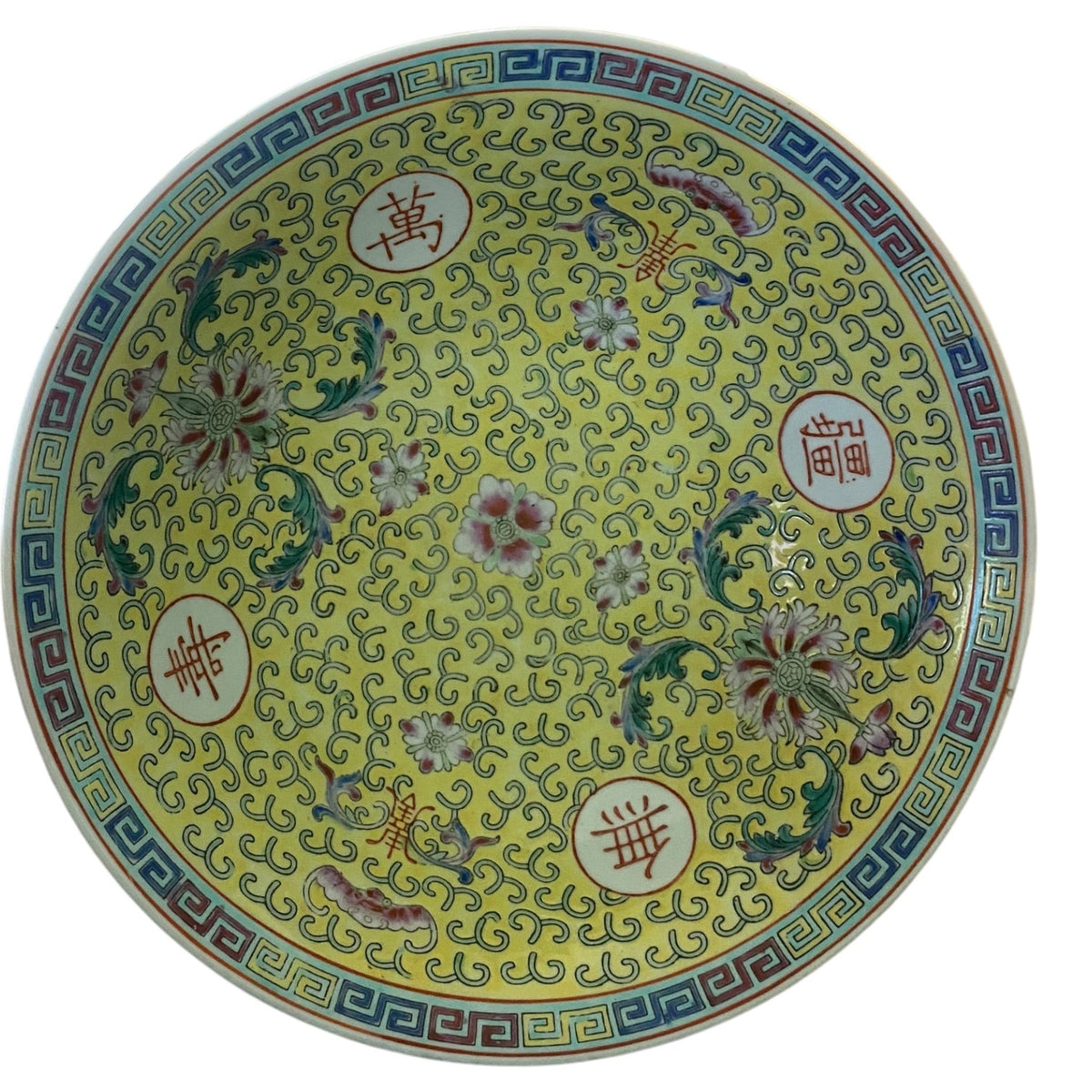 A round bowl with a yellow glaze, decorated with intricate floral motifs, scrolling patterns, and Chinese characters inside white circles, set against a plain white background.