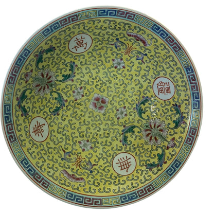 A round bowl with a yellow glaze, decorated with intricate floral motifs, scrolling patterns, and Chinese characters inside white circles, set against a plain white background.