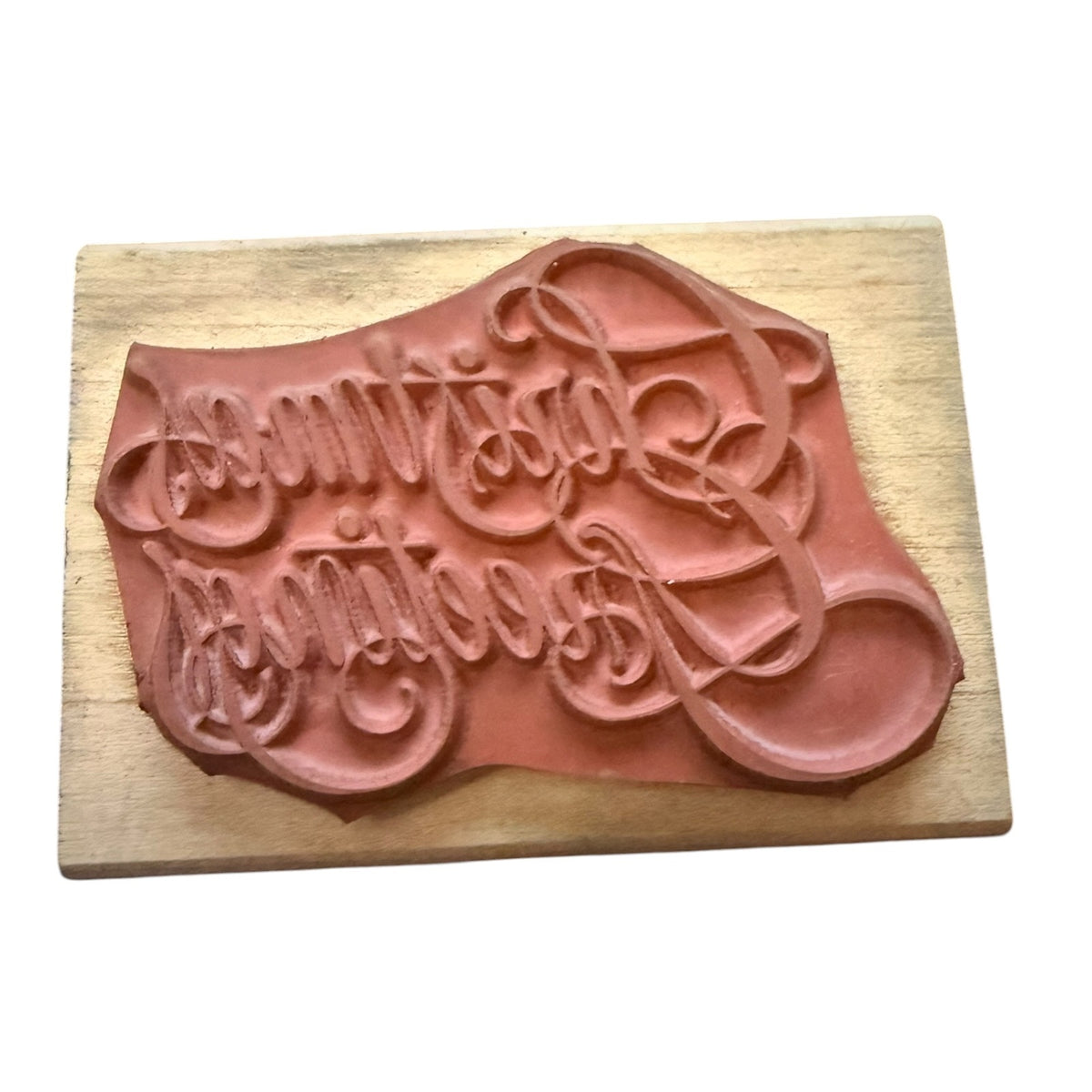 A terracotta-colored clay stamp with elegant cursive lettering, mounted on a rectangular light wood block against a plain white background.