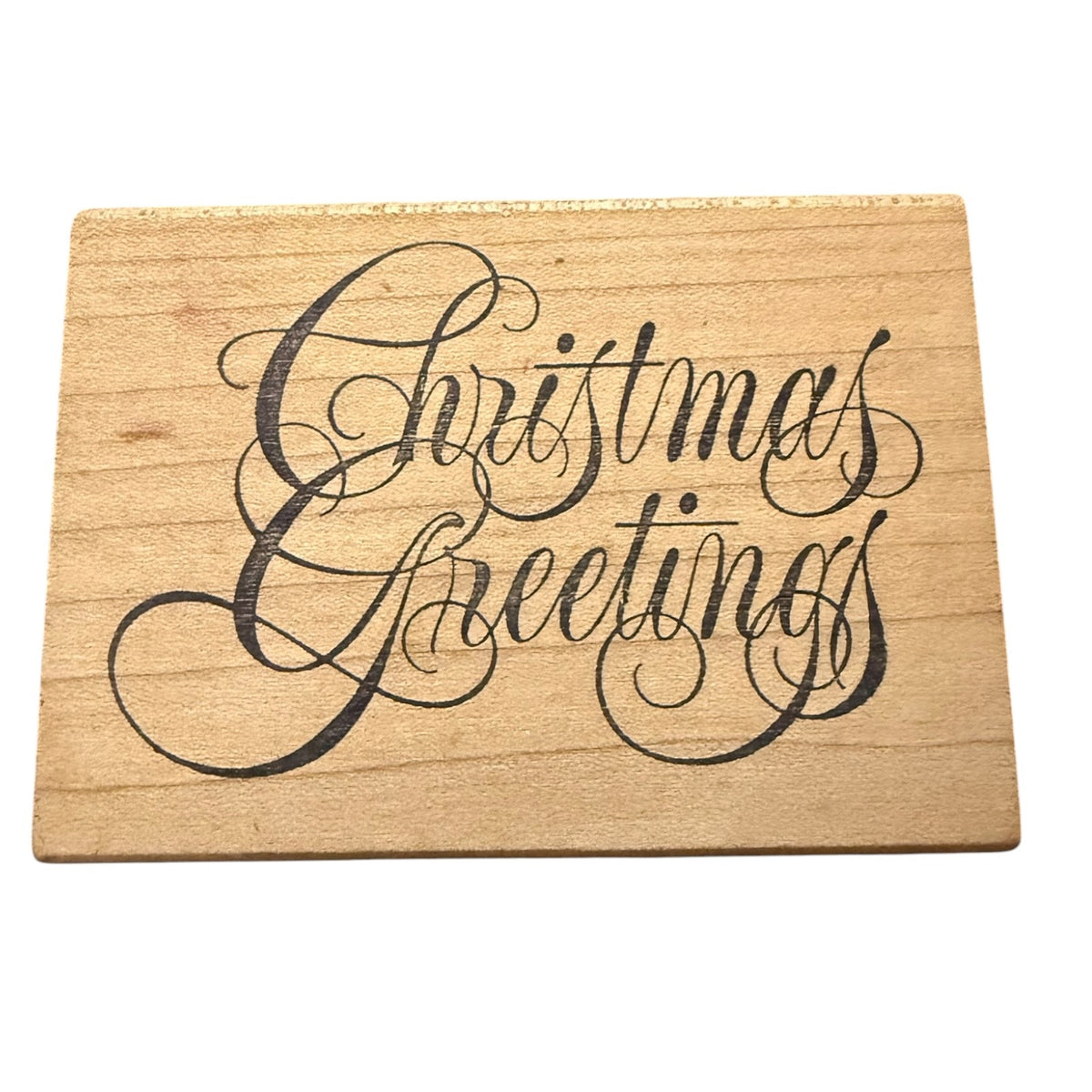 A rectangular wooden stamp with the words 'Christmas Greetings' written in large black cursive script, shown on a plain white background.