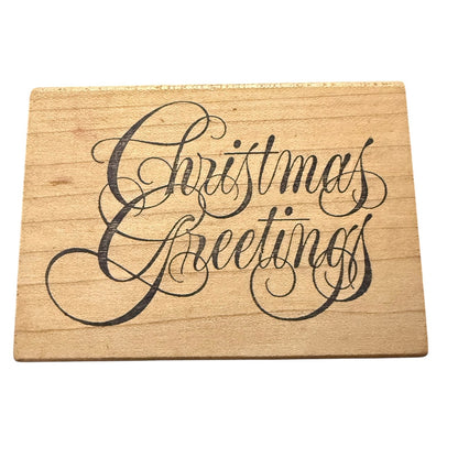 A rectangular wooden stamp with the words 'Christmas Greetings' written in large black cursive script, shown on a plain white background.