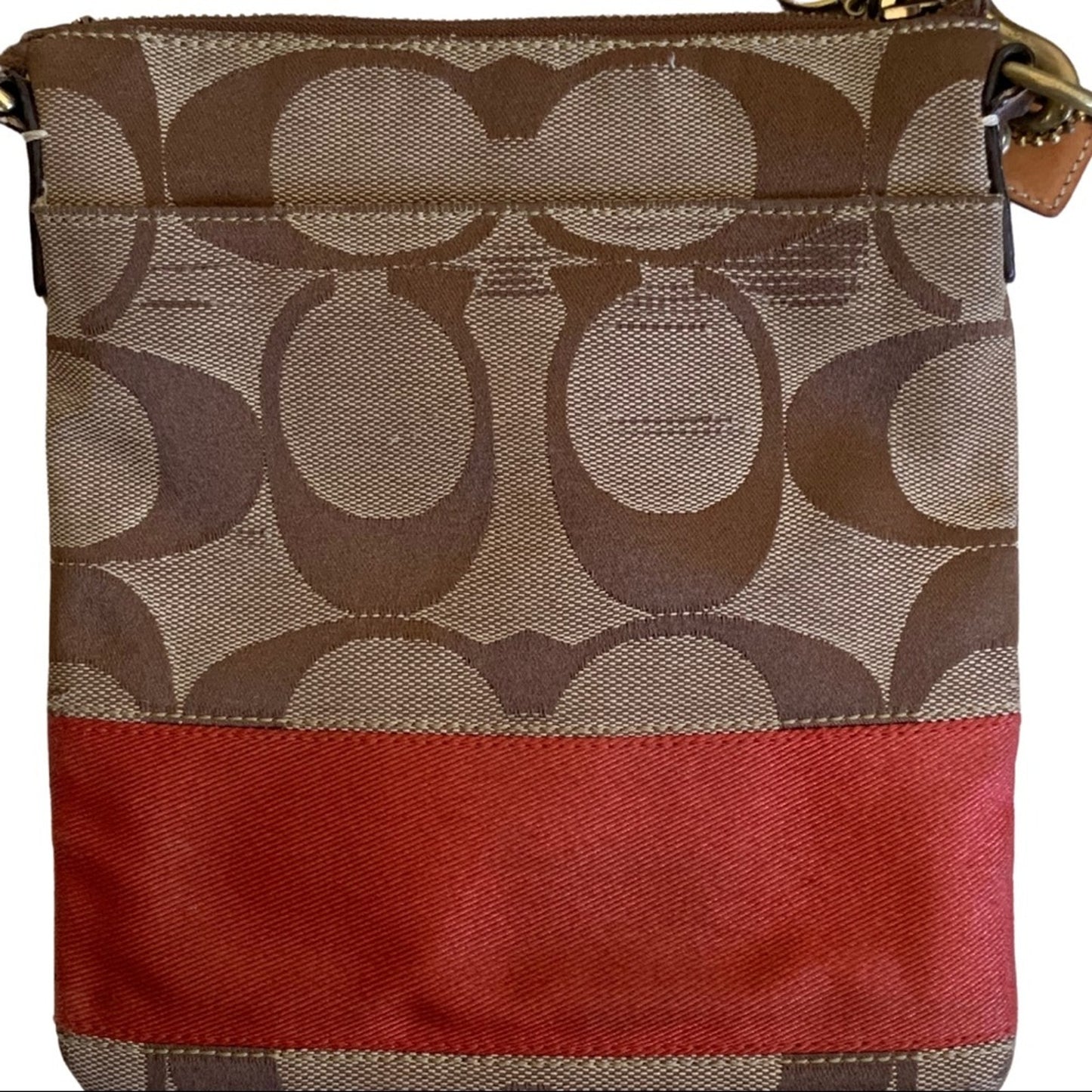 A close-up of a Coach crossbody bag featuring the signature brown monogram pattern on the upper portion and a solid orange horizontal stripe across the lower portion.