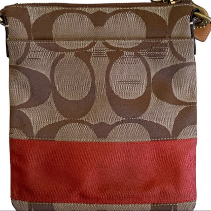 A close-up of a Coach crossbody bag featuring the signature brown monogram pattern on the upper portion and a solid orange horizontal stripe across the lower portion.