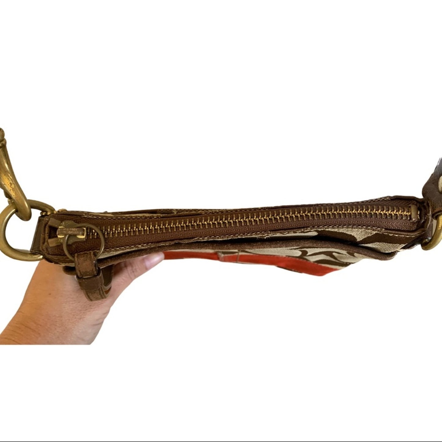 A close-up of a brown leather zippered pouch held by a hand, showing a gold-tone metal clasp .