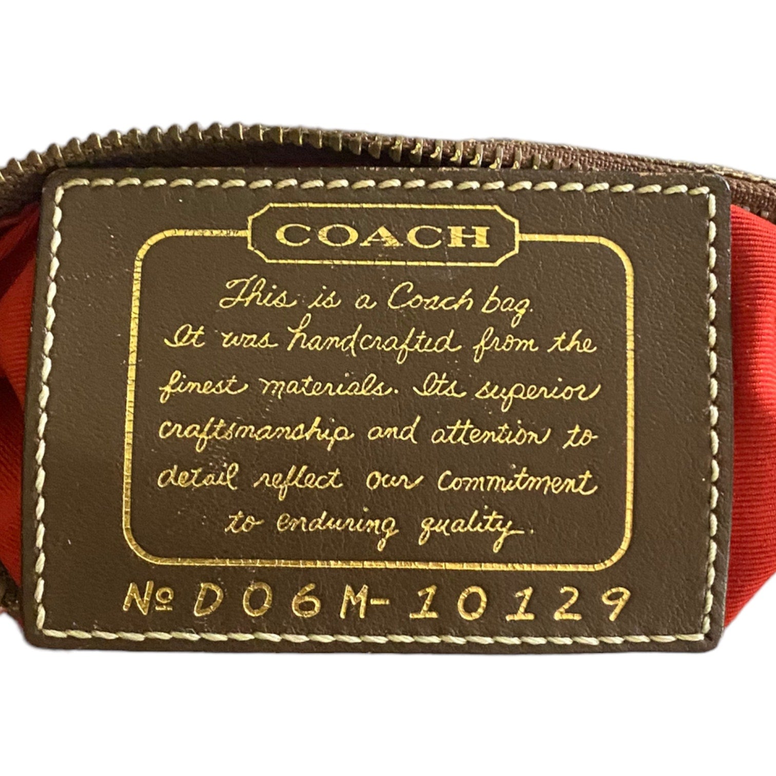 Close-up of a Coach leather tag on a brown bag, featuring gold-embossed lettering and a orange fabric lining visible at the sides.